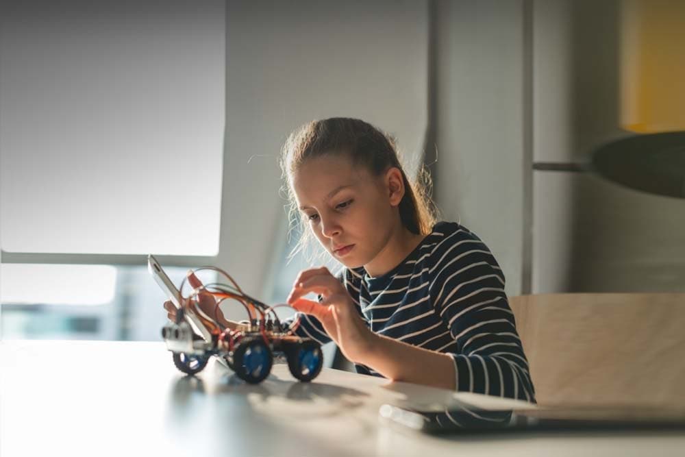 Young female student in a striped shirt enjoying her STEM class at Georgia Connections Academy and working on the electronic toy