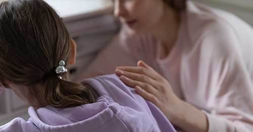 Image of a a parent in a pink sweater shirt supporting their child.